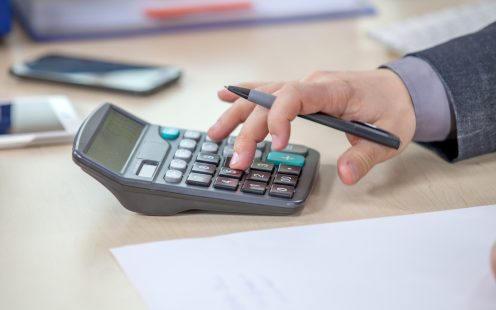 egy asztalnál kézi számológépen kalkulációt végez egy férfi kéz
